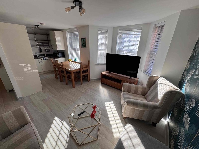 Open-plan living room with sofa, armchair, TV, dining table and kitchen area visible