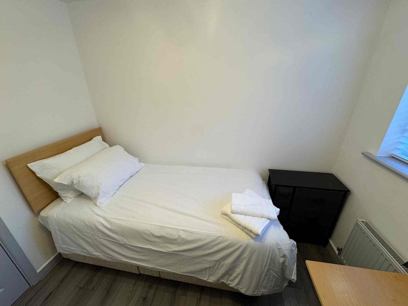 Small bedroom with single bed, white bedding, wooden frame and dark storage box