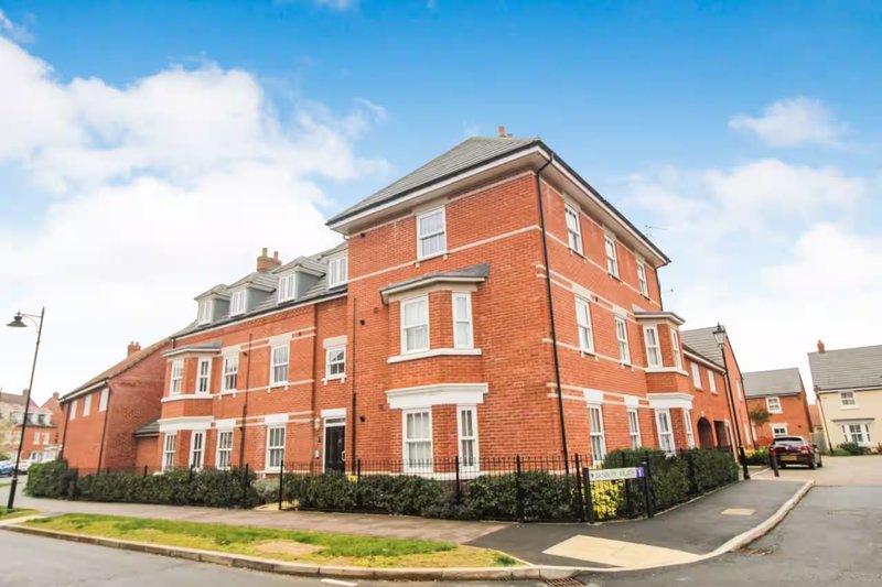 Red brick corner building with multiple windows, black roof trim, and front garden