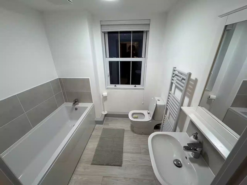 Modern bathroom with bathtub, toilet, sink, heated towel rail and window