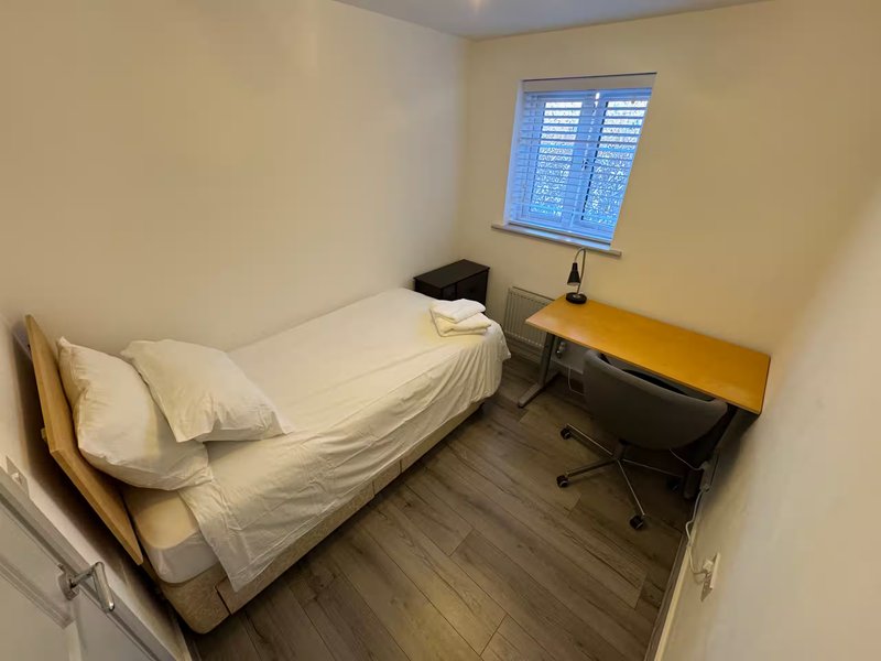 Compact bedroom with single bed, wooden desk, chair and window with shutters