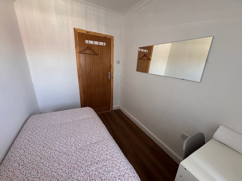 Small bedroom with single bed, wooden door, mirror, and dark wooden flooring