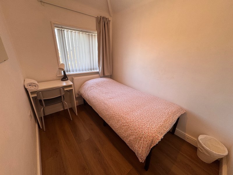 Small bedroom with single bed, wooden desk, vertical blinds window and wooden flooring