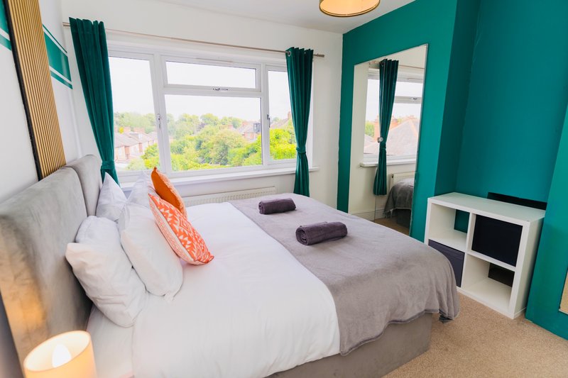 Modern bedroom with double bed, teal accent wall, large windows and mirrored wardrobe