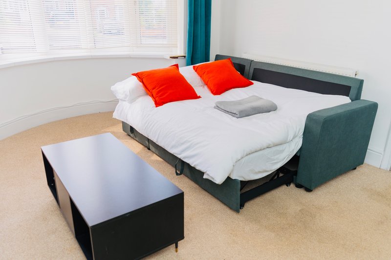 Bright bedroom with curved sofa bed, white bedding, orange pillows and coffee table