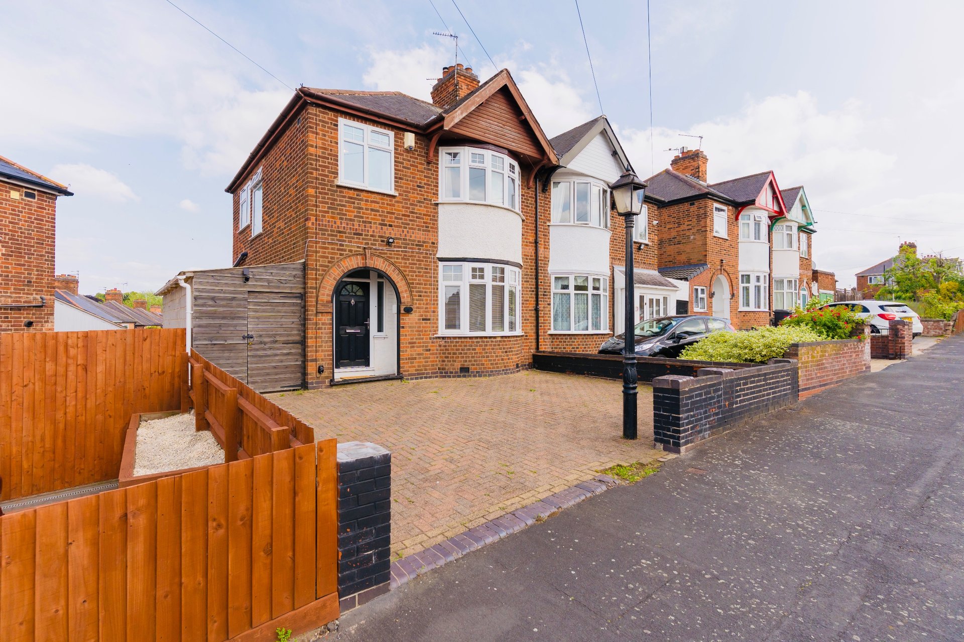 Brick semi-detached house with driveway, front garden, and wooden fence