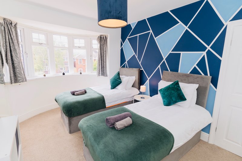 Twin bedroom with geometric blue accent wall, green velvet cushions and throws, white bedding, pendant light