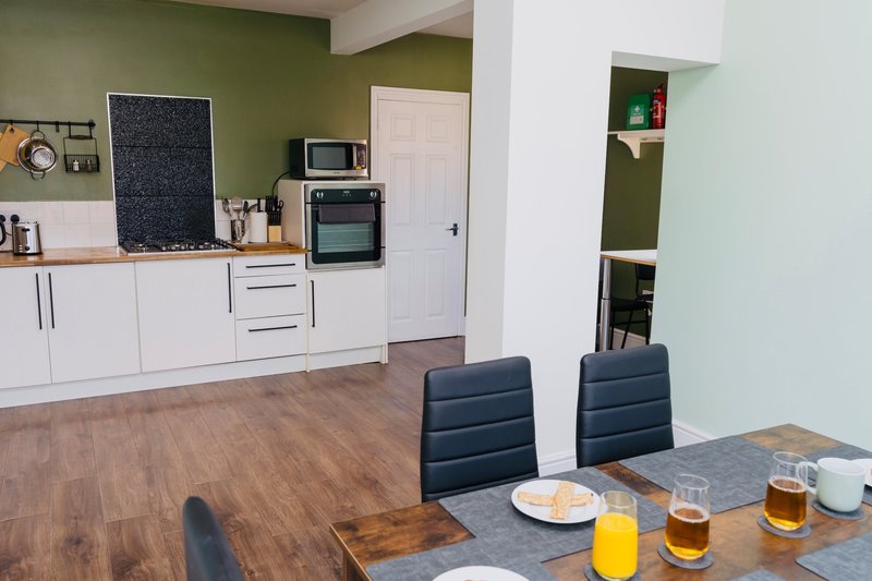 Open-plan kitchen and dining area with white cabinetry, green accent wall, and dining table