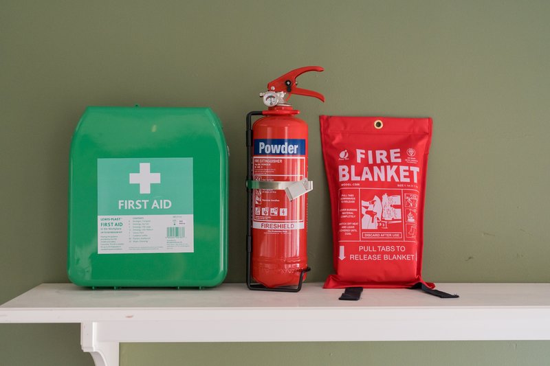 Shelf with green first aid kit, red powder fire extinguisher, and red fire blanket