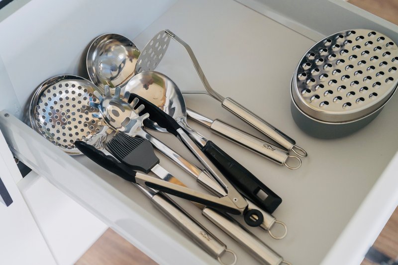 Kitchen drawer with cooking utensils including graters, slotted spoons, and metal tools