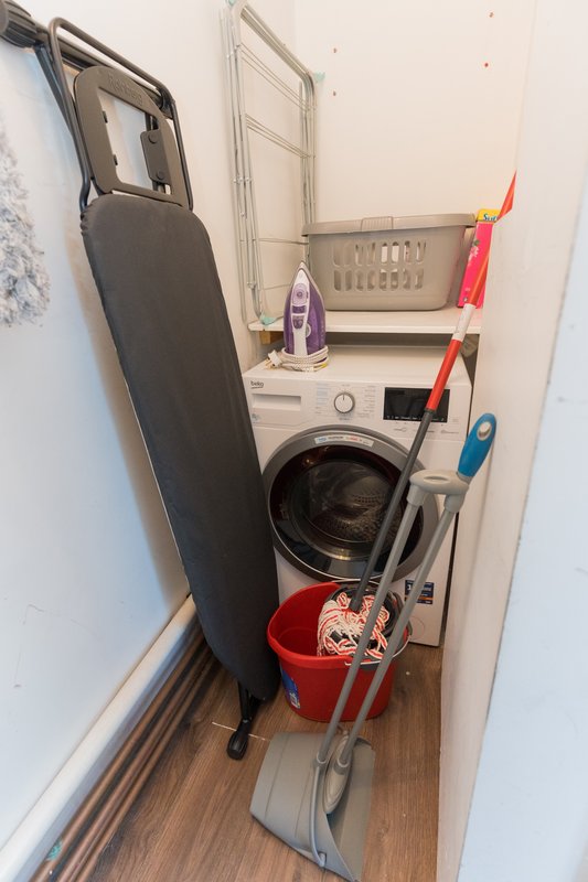Compact laundry room with washing machine, ironing board, and cleaning supplies