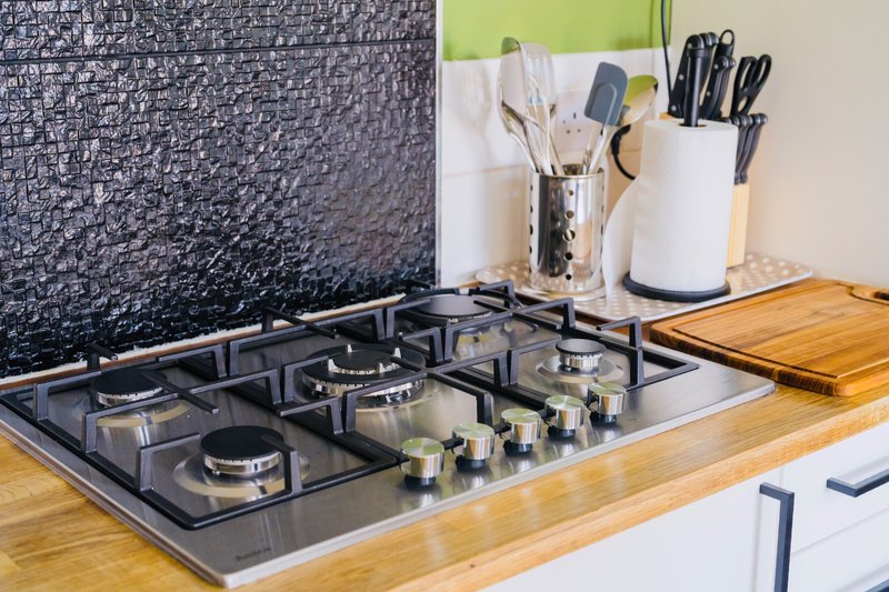 Modern kitchen countertop with gas cooktop, utensil holders, and wooden counters