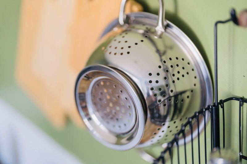 Close-up of stainless steel colander hanging on kitchen wall rail