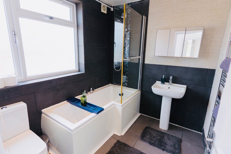 Modern bathroom with white bathtub, shower enclosure, pedestal sink and window