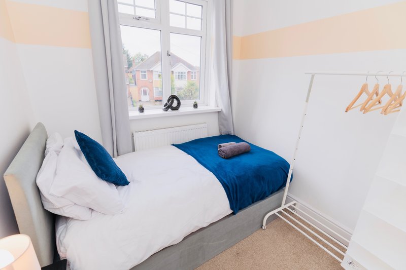 Bright bedroom with single bed, blue bedding, white pillows, and window view