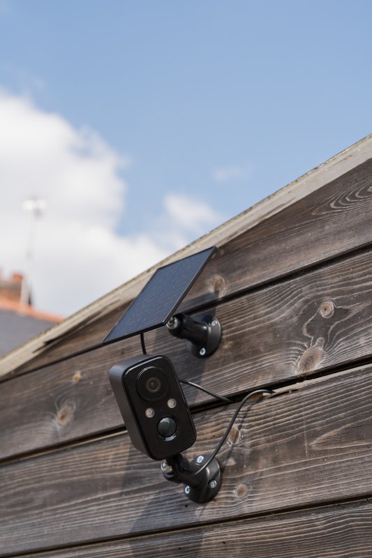 Solar-powered security camera mounted on wooden exterior wall against blue sky