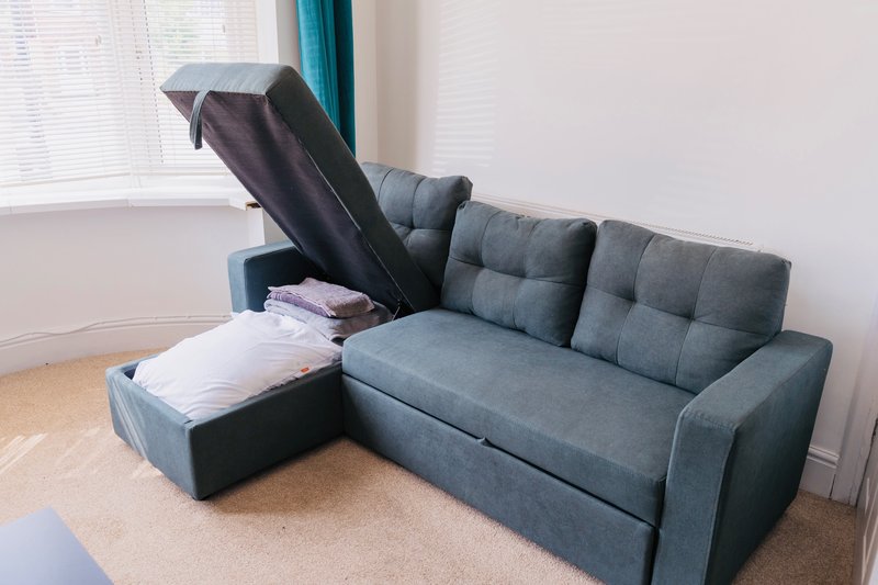 Gray upholstered corner sofa with storage compartment open, showing bedding inside