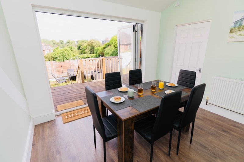 Dining room with dark wooden table, black chairs, and glass doors opening onto garden