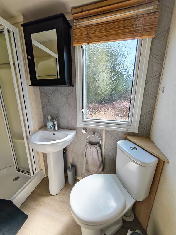 Compact bathroom with toilet, pedestal sink, mirror cabinet and window overlooking garden