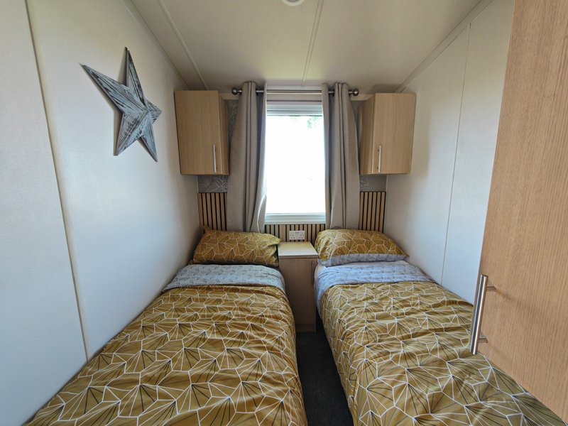 Twin bedroom with two single beds, wooden wardrobes, window with grey curtains, and decorative star