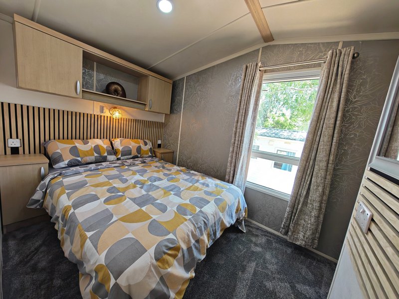 Bedroom with double bed, geometric patterned duvet, wooden storage cabinets and glass door to deck