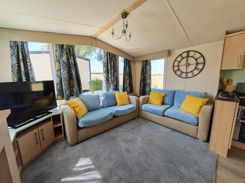 Open-plan living area with two sofas, TV, large windows and decorative clock