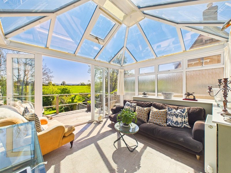 Bright conservatory with black sofa, patterned cushions, yellow chair and countryside views