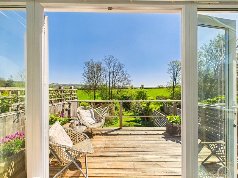 Wooden deck with wicker chairs overlooking green countryside and fields