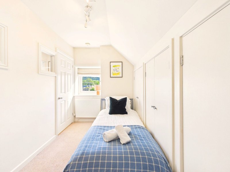 Narrow bedroom with single bed, blue checkered duvet, black pillow, cream carpet and white doors