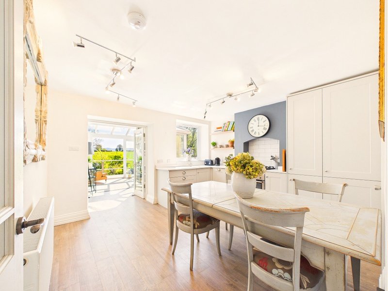 Bright open-plan kitchen and dining area with white cabinetry, wooden table, and garden view