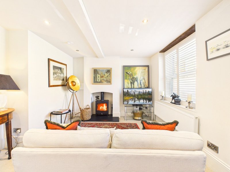 Bright living room with cream sofa, wood-burning stove, framed artwork, and orange accent cushions