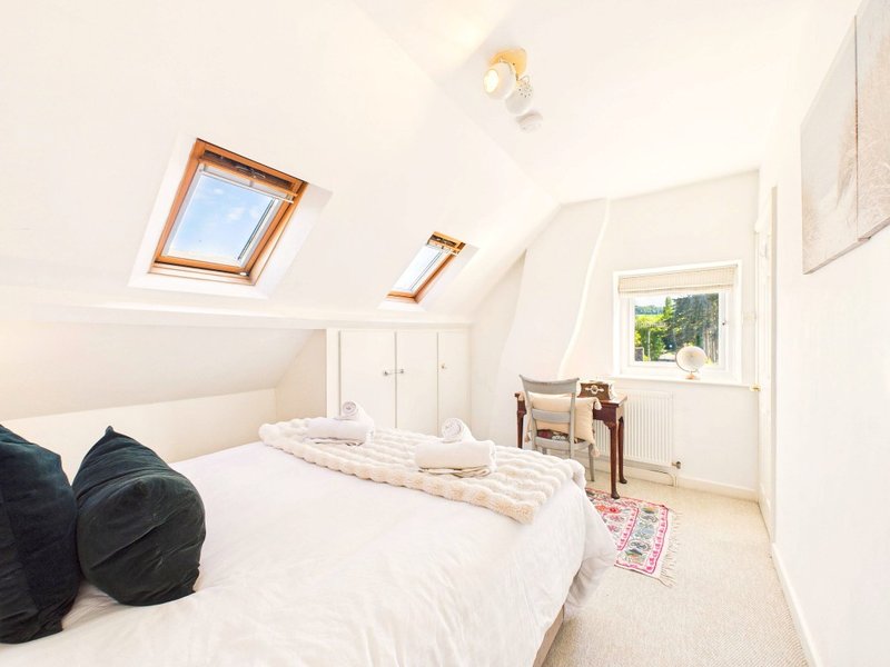 Bright attic bedroom with skylights, double bed, black cushions and cream bedding