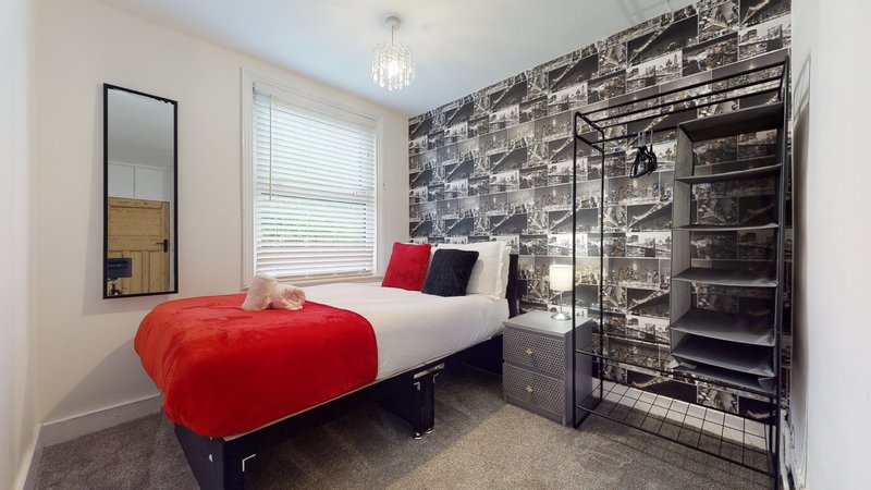 Bedroom with double bed, red blanket, industrial-style wallpaper, and mirror