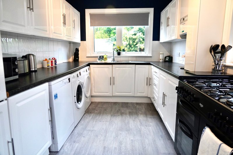 Modern kitchen with white cabinetry, black countertops, gas range and window overlooking garden