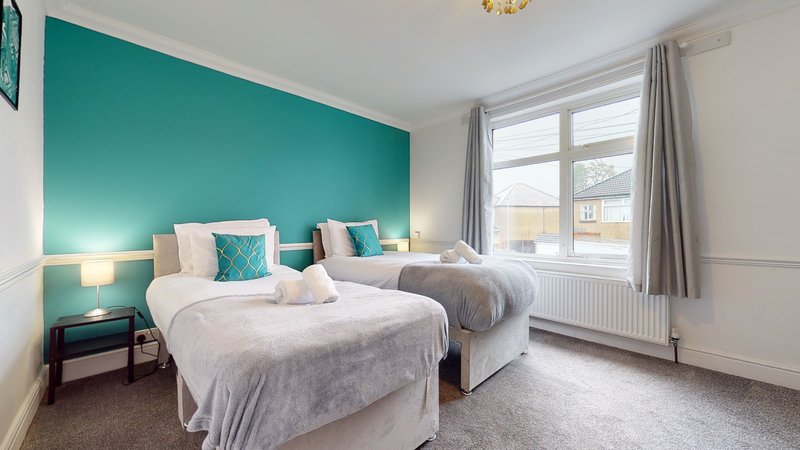 Bright twin bedroom with teal accent wall, two beds with white bedding, bedside lamps and large window