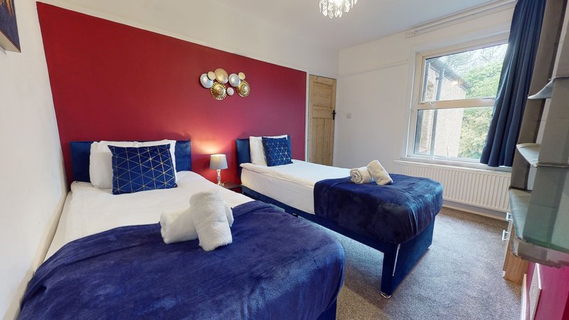 Bedroom with two twin beds, navy velvet bedding, red accent wall, and large windows