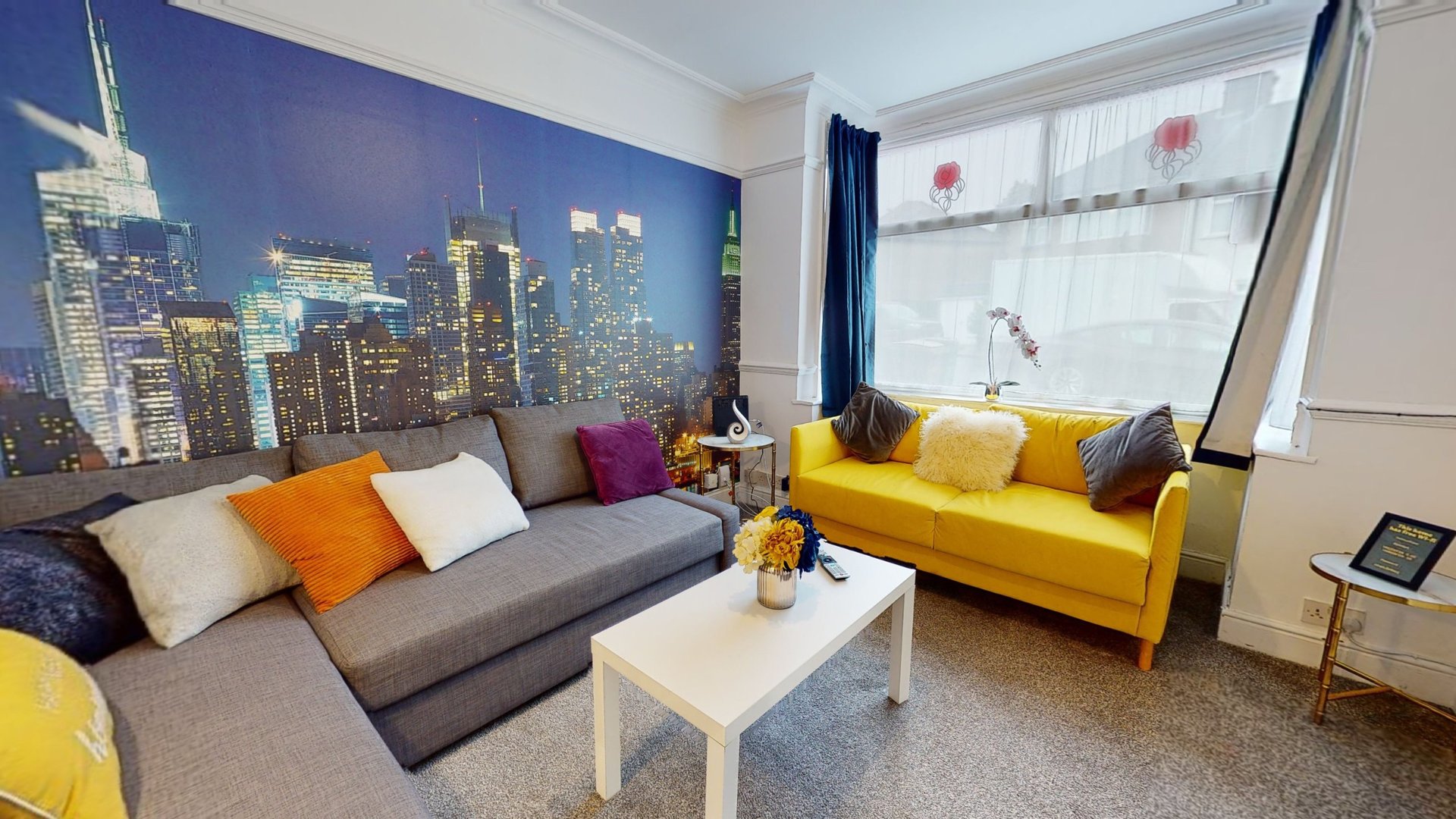 Bright living room with gray corner sofa, yellow armchair, cityscape wall mural, and white coffee table