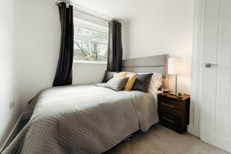 Bedroom with double bed, grey headboard, black curtains, bedside lamp and wooden nightstand