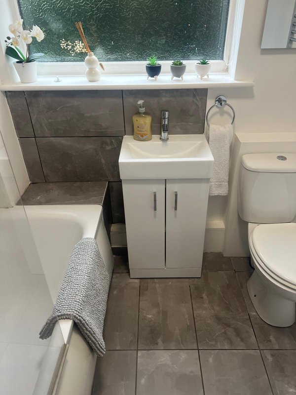 Modern bathroom with white vanity, toilet, sink, and tiled flooring near window
