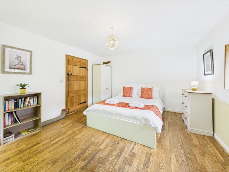Bright bedroom with double bed, wooden floor, bookshelf, and white furniture