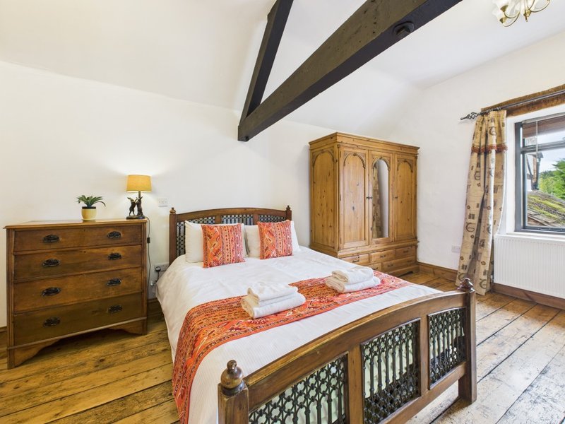 Rustic bedroom with wooden bed, orange bedding, chest of drawers and exposed beams