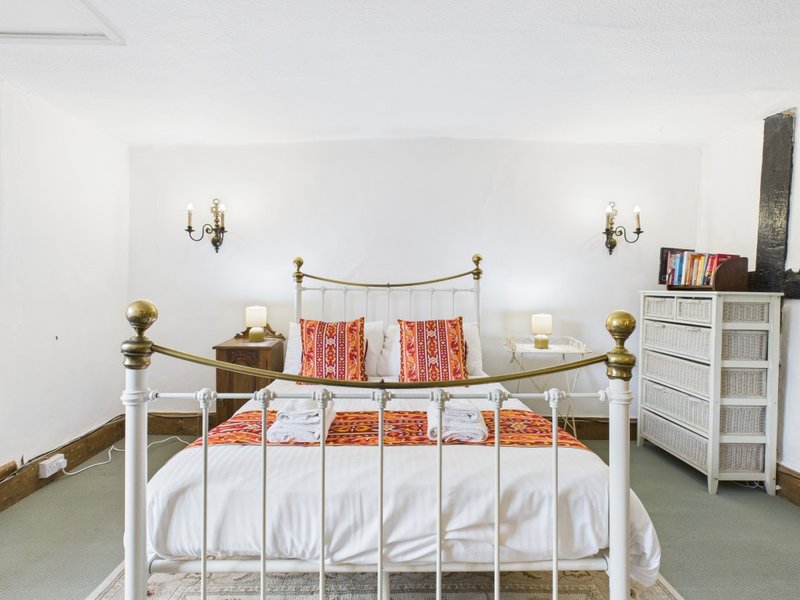 Bright bedroom with white metal bed frame, orange patterned pillows, wall sconces, and white storage furniture