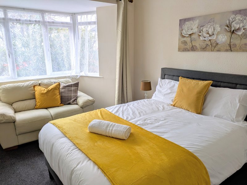 Comfortable double bedroom ideal for working guests, featuring a spacious bed, fresh linen, a cosy sofa and a bright bay window. A relaxing space to unwind after a busy day, with a homely feel