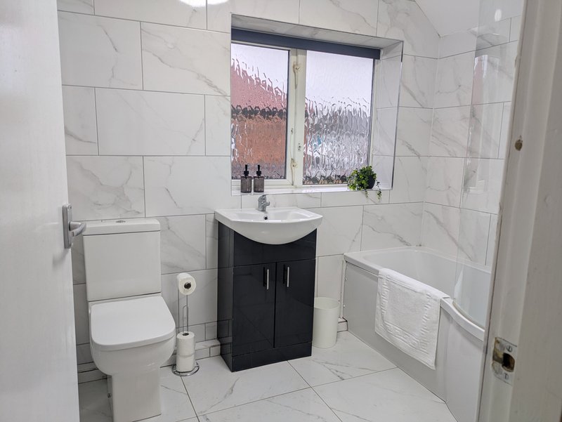 Modern, bright bathroom with a full-size bath and shower, clean tiled finish, vanity unit and fresh towels, ideal for contractors wanting a comfortable, well-equipped home-from-home after a busy day.