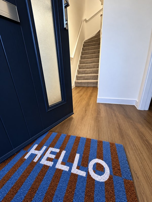Entrance hallway with navy blue door, wooden floor, striped welcome mat and staircase