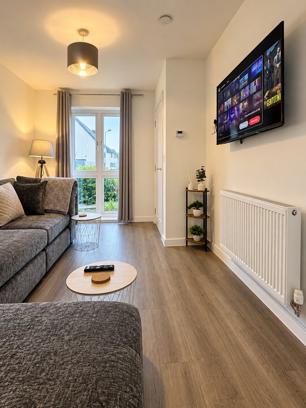 Modern living room with grey sofas, wall-mounted TV, wooden flooring and patio doors