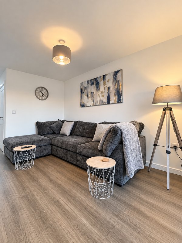 Living room with dark corner sofa, wooden floor, tripod floor lamp and wall art
