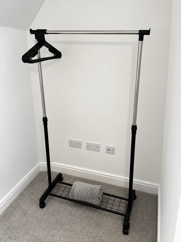 Freestanding clothing rail with hanger and cable storage in empty bedroom corner
