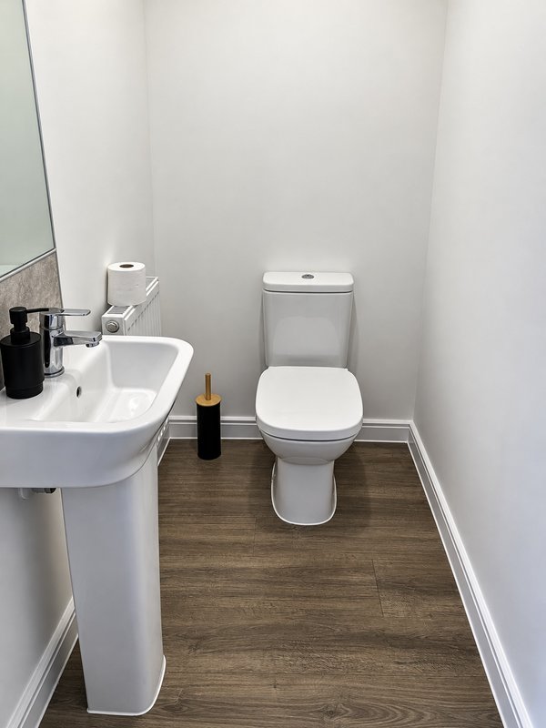 Small bathroom with pedestal sink, toilet, mirror and wooden floor