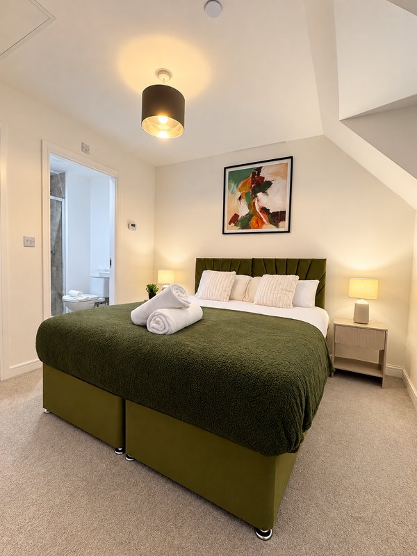 Bedroom with olive-green bed, framed artwork, ceiling light, and bedside lamps